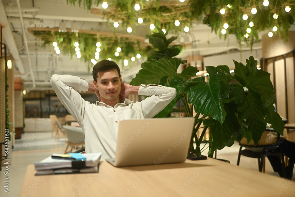Satisfied businessman taking a break from computer work relaxing at table in office lounge Satisfied businessman taking a break from computer work relaxing at table in office lounge