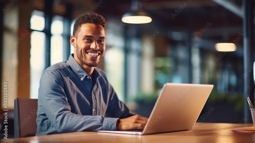 A man smiles while working on his laptop in a modern office setting A man smiles while working on his laptop in a modern office setting