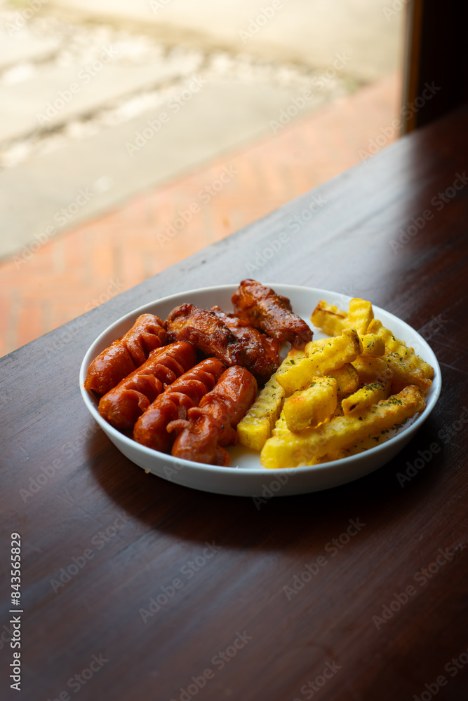 mixed sausage, french fries, and chicken wings cafe platter. Served on white plate, over wooden table surface, in cafe environment mixed sausage, french fries, and chicken wings cafe platter. Served on white plate, over wooden table surface, in cafe environment