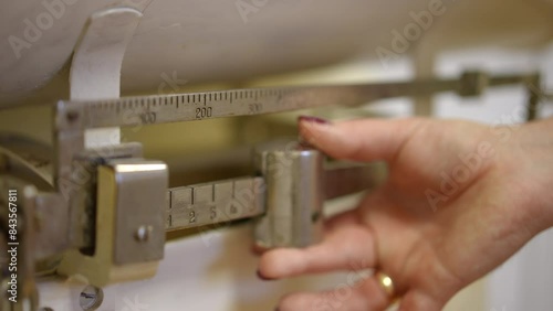 Slow motion. Close-up of the weighing process on a medical mechanical scale for newborns in a city clinic. A woman's hand moves a metal counterweight along a metal scale photo