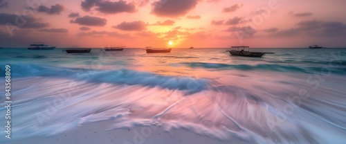 Sunset over the sea with boats on the beach.