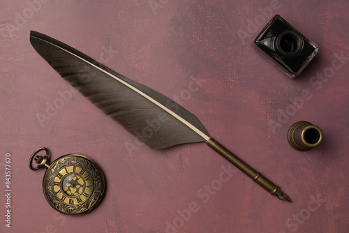 Old quill pen, ink and vintage watch on a burgundy background. Retro style. Top view