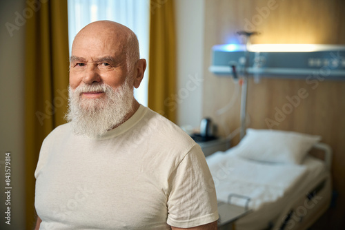 Old man looking at camera near hospital bed