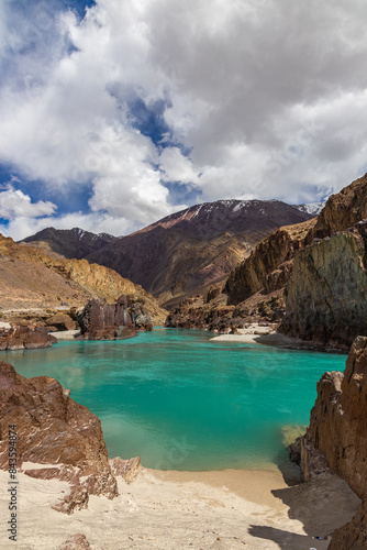 Landscape of sandy beaches amidst Jagged Mountain rocks and clear green water In Ladakh.