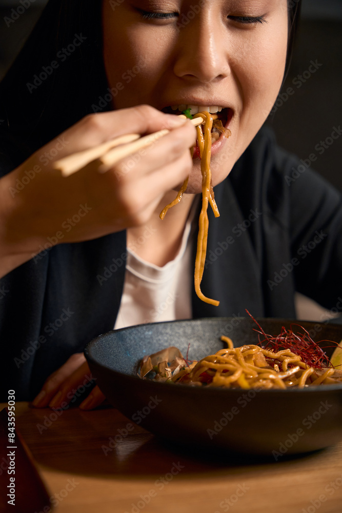 Close-up young Asian woman eating noodles in ginger-honey sauce with chopsticks