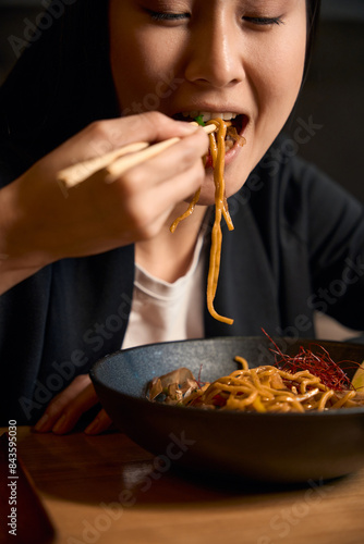 Obraz na płótnie Close-up young Asian woman eating noodles in ginger-honey sauce with chopsticks w salonie