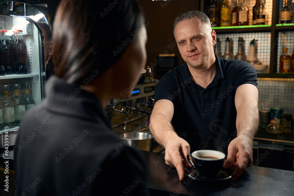 Handsome barman treating brunette woman with cup of freshy brewed coffee Handsome barman treating brunette woman with cup of freshy brewed coffee