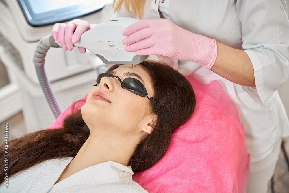 Naklejka premium Young woman undergoing intense pulsed light therapy done by beautician