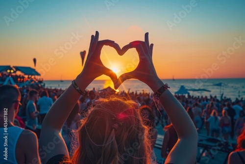 Concertgoer forms heart shape with hands at beachside music festival, crowd enjoys live performance in sunset, love symbol gesture at summer event, youth celebration of art outdoor entertainment photo