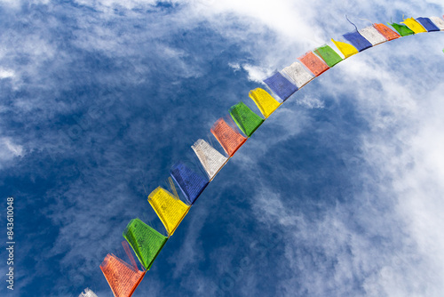Colorful Tibetan prayer flags attached to a string flying in air against blue sky with clouds   