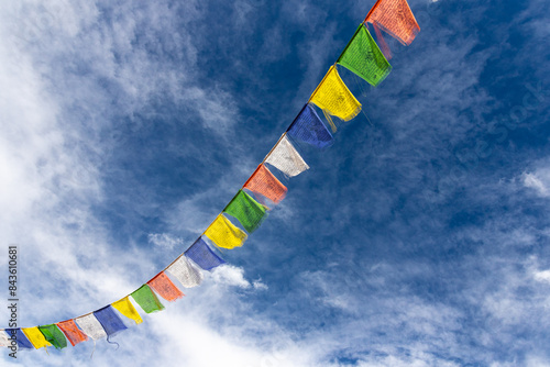 Colorful Tibetan prayer flags attached to a string flying in air against blue sky with clouds   