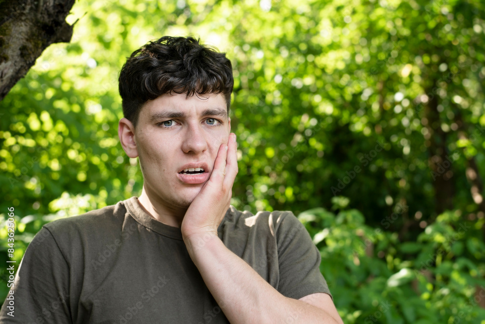 A young guy felt a strong toothache while running in nature, grimaces and holds cheek, dental concept. A young guy with an athletic build has a toothache A young guy felt a strong toothache while running in nature, grimaces and holds cheek, dental concept. A young guy with an athletic build has a toothache