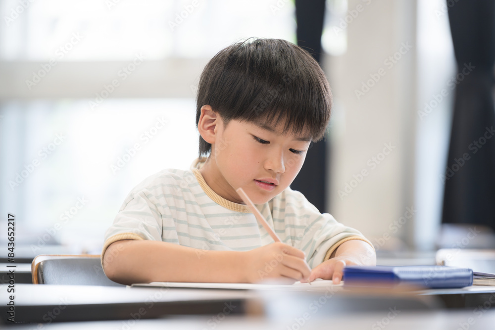 An elementary school boy studying and holding a pencil during class in a classroom An elementary school boy studying and holding a pencil during class in a classroom