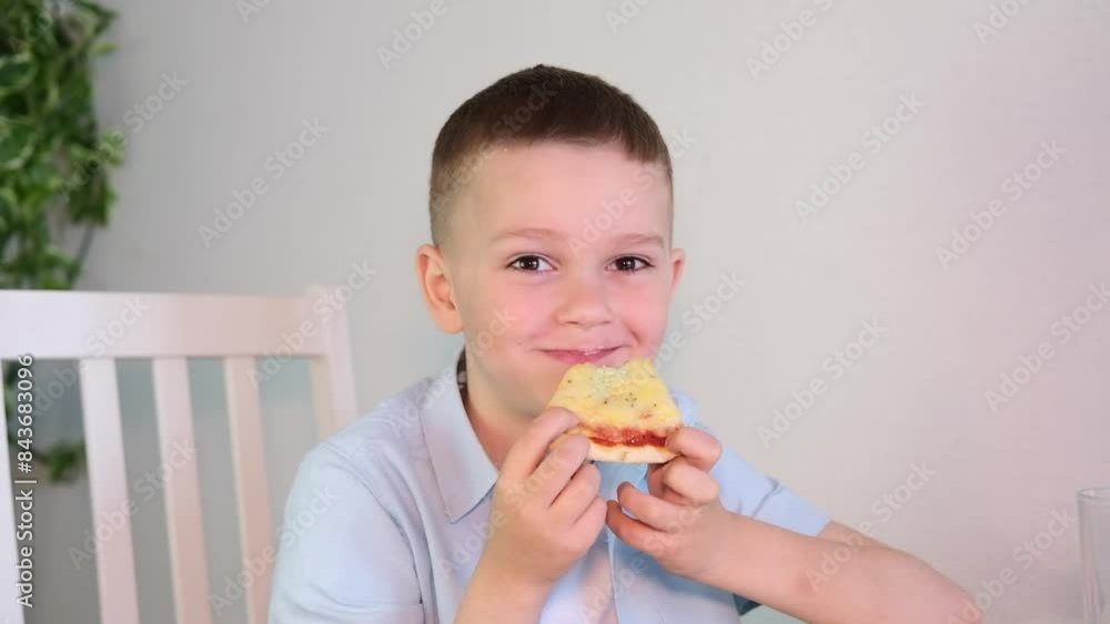 Happy little boy enjoying lunch eating a piece of pizza at home in the kitchen. Children love junk food. Baby food concept. Selective focus. Happy little boy enjoying lunch eating a piece of pizza at home in the kitchen. Children love junk food. Baby food concept. Selective focus.