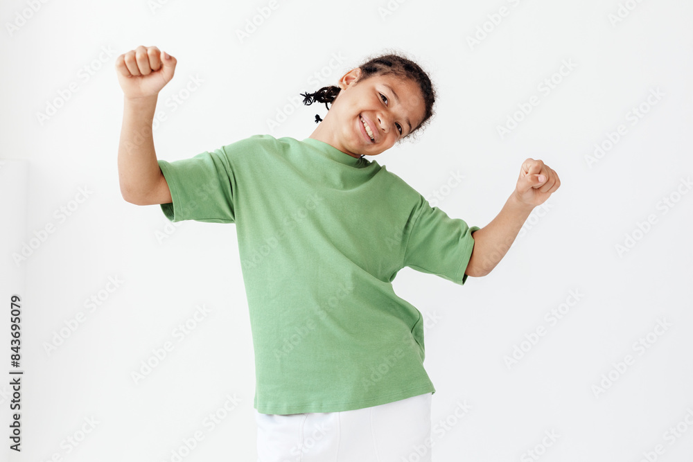 Fototapeta premium Excited young boy in stylish outfit raises arms in celebration against a green background
