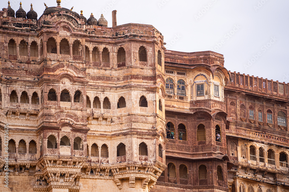 Fototapeta premium majestic stone walls of mehrangarh fort with window arches in jodhpur sitting on top of hill surrounded by monsoon clouds with birds flying around this landmark of rajput warrior history