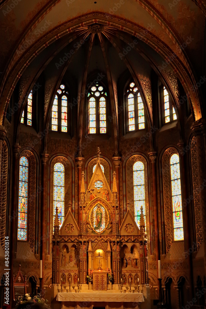 Fototapeta premium Elaborate altar in front of stained glass windows in gothic style shape inside the Matthias Church, Budapest, Hungary
