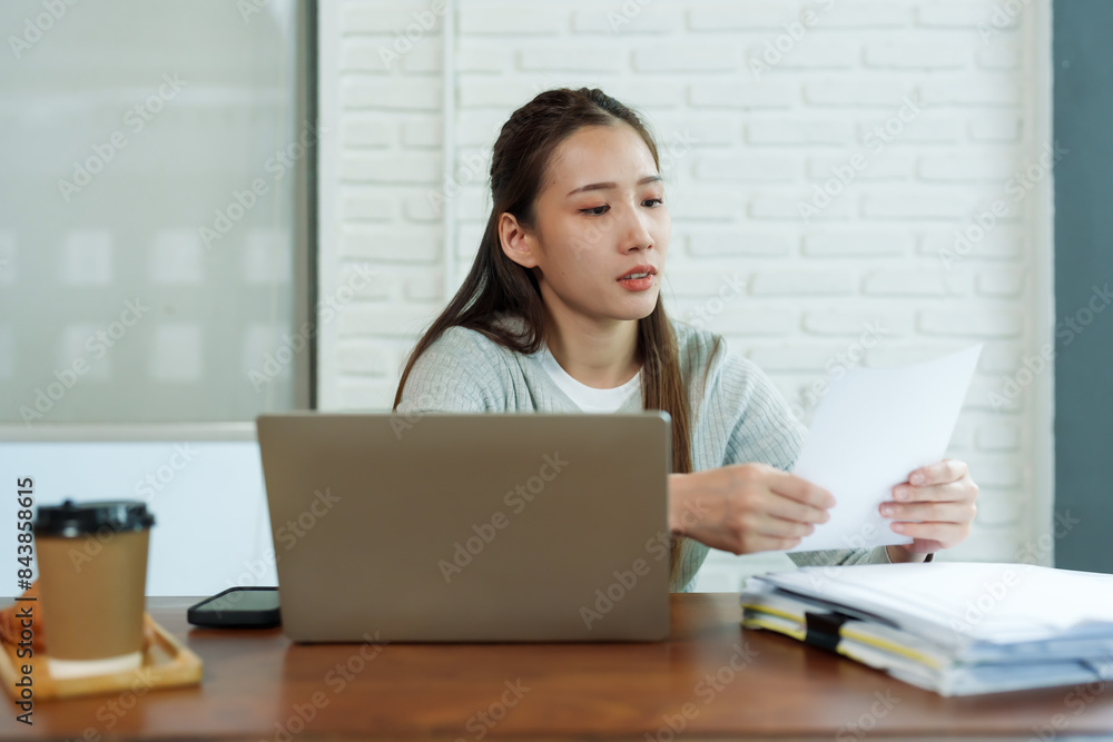Beautiful young Asian female barista sitting at table in coffee shop Stressed about checking the store's accounts with laptop computer Drink coffee in afternoon to keep yourself from feeling sleepy. Beautiful young Asian female barista sitting at table in coffee shop Stressed about checking the store's accounts with laptop computer Drink coffee in afternoon to keep yourself from feeling sleepy.