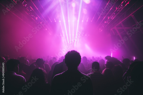 vibrant crowd of people is silhouetted against a backdrop of purple and pink lights at a concert or music festival. The energy of the event is palpable