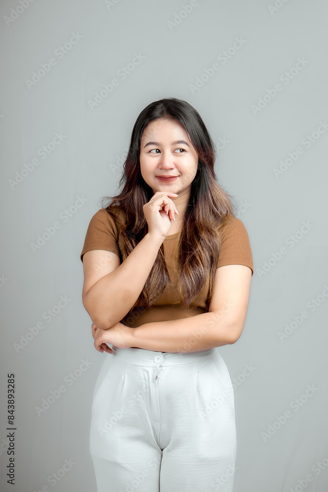 Studio portrait of a beautiful young Asian Indonesian woman thinking about something while standing and holding her chin. Isolated Studio portrait of a beautiful young Asian Indonesian woman thinking about something while standing and holding her chin. Isolated