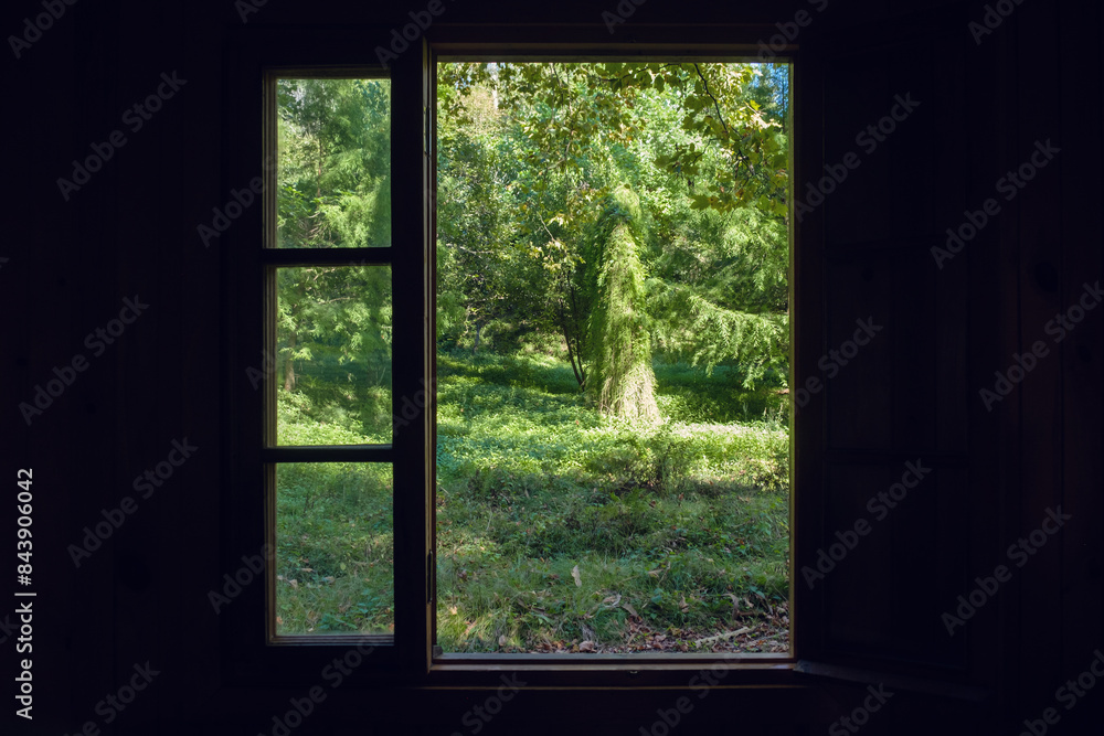Looking through the window in the dark room can see the beautiful view of the garden lit by sunlight Looking through the window in the dark room can see the beautiful view of the garden lit by sunlight