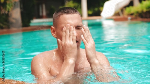 teenage boy swims out of chlorinated water in an open-air pool wiping his eyes from water.slow motion.