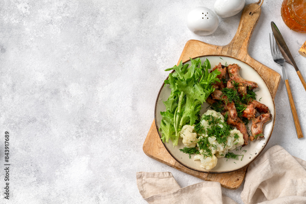 Baked or fried chicken necks in barbecue sauce, cauliflower and lettuce leaves on a plate on the table. A healthy dinner on a light gray background. Proper nutrition. Top view from the copyspace