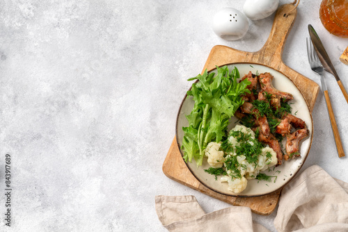 Obraz na płótnie Baked or fried chicken necks in barbecue sauce, cauliflower and lettuce leaves on a plate on the table. A healthy dinner on a light gray background. Proper nutrition. Top view from the copyspace w salonie