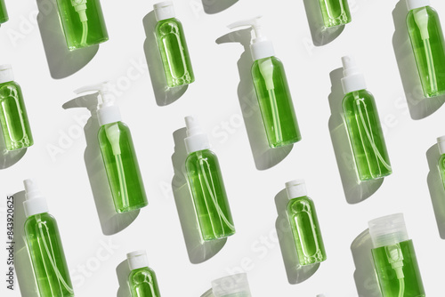 Transparent different plastic bottles with green liquid as trend minimal pattern, skin care, beauty and wellness, body treatment products on light background at sunlight, top view, aesthetic flatly photo