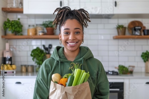 asian couple in green hoodies with paper bag full of vegetables standing in minimal kitchen smiling after grocery shopping at eco market, 0km food concept photo