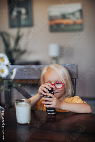 Little blond girl with red glasses with a glass of molk and oreo cookies