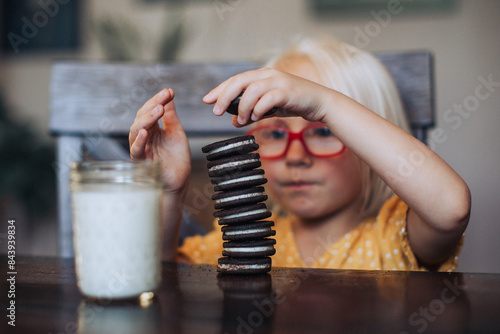 Little blond girl with red glasses with a glass of molk and oreo cookies