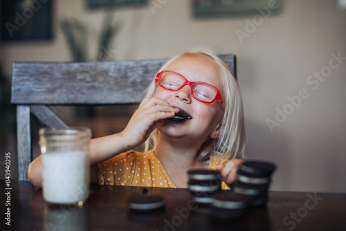 Little blond girl with red glasses with a glass of molk and oreo cookies photo