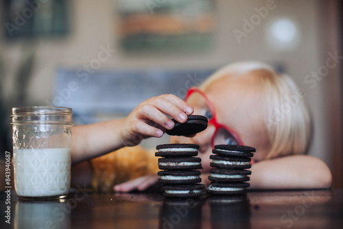 Little blond girl with red glasses with a glass of molk and oreo cookies
