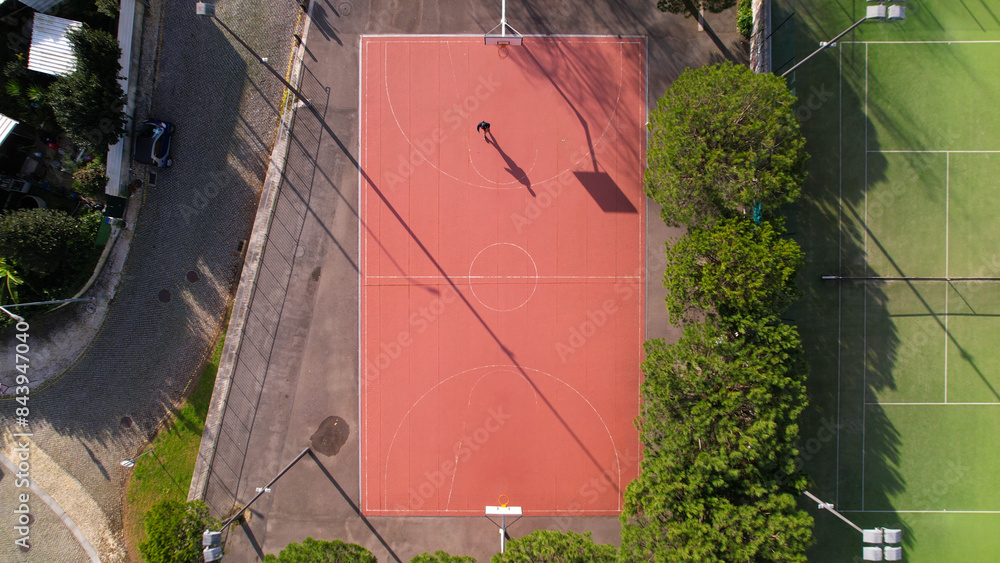DRONE AERIAL VIEW: Man practicing basketball outside. Male sportsman playing basketball throwing the ball at the playground.