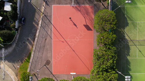 Obraz na płótnie DRONE AERIAL VIEW: Man practicing basketball outside. Male sportsman playing basketball throwing the ball at the playground. w salonie