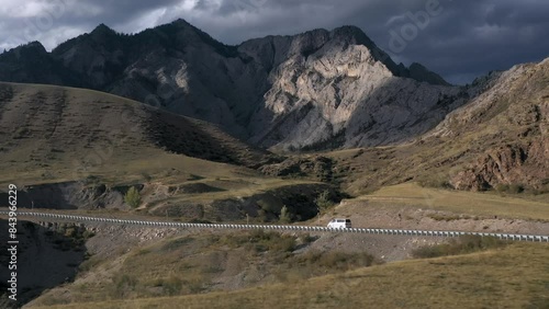 White van automobile driving on rocky mountain asphalt road at sunny cliff highland drone side shot. Auto vehicle travel trip natural sunlight hilly terrain blue sky. Transportation adventure 4k video photo