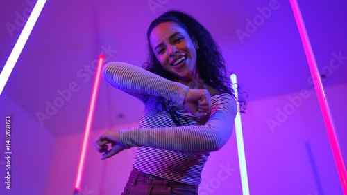 Low angle camera of hispanic dancer looking at camera and dancing to city pop music. Professional attractive hipster moving to hip hop song with purple led or neon light. Stylish cloth. Regalement. photo