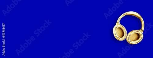 Big modern golden headphones isolated on blue background. Minimal concept. Copy space for the text