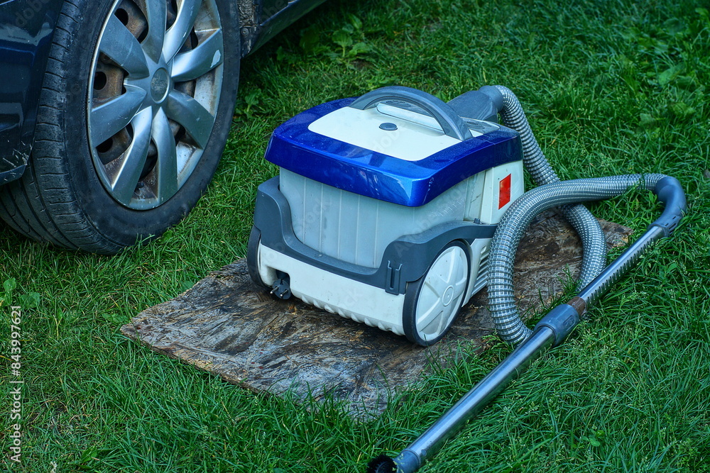 one modern compact plastic on wheels multi-colored modern electric home powerful vacuum cleaner for cleaning dust stands on the street in the green grass during the day one modern compact plastic on wheels multi-colored modern electric home powerful vacuum cleaner for cleaning dust stands on the street in the green grass during the day