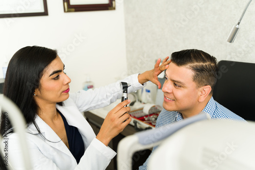 Hispanic woman ophthalmologist using an ophthalmoscope to examine the eyes of a willing male patient in a clinical setting photo