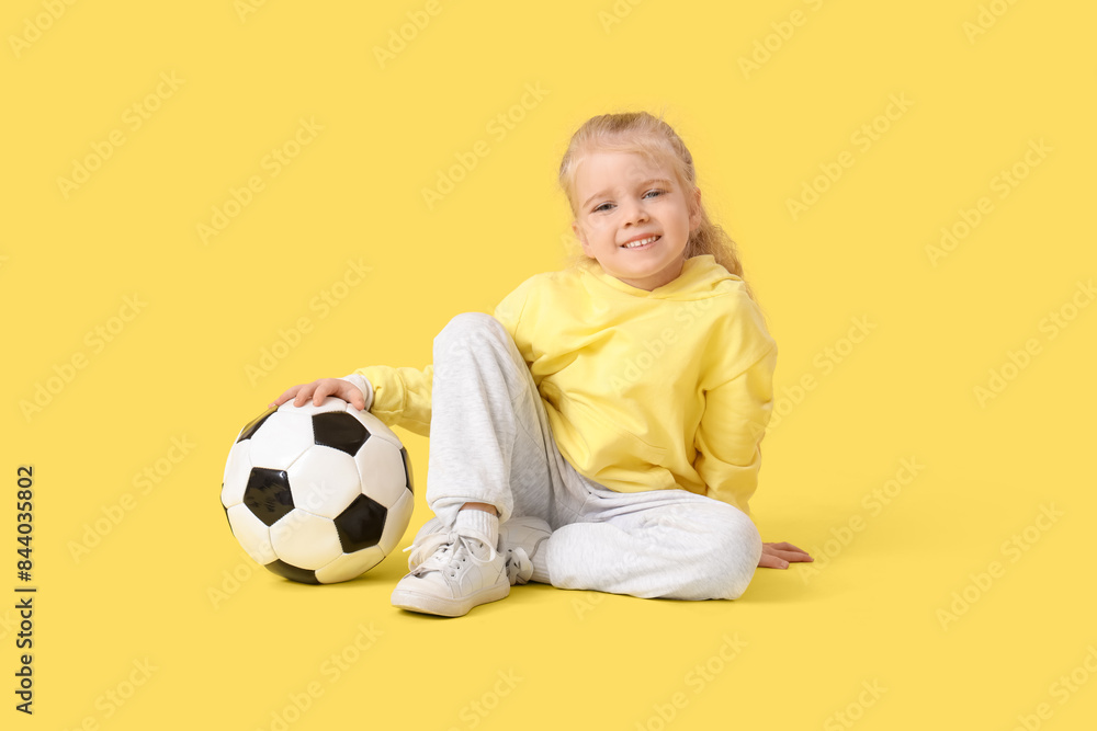 Cute little girl with soccer ball sitting on yellow background Cute little girl with soccer ball sitting on yellow background
