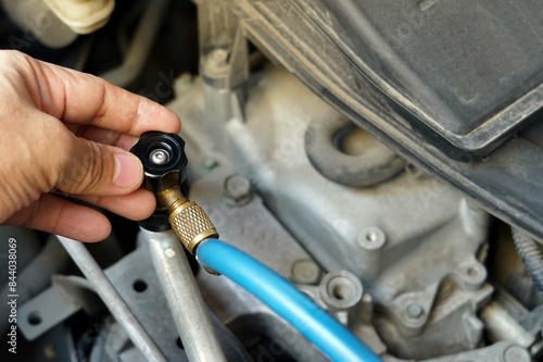 Close up a hand is coonecting a refrigeration charging hoses connect with a tube to an air car compressor. photo