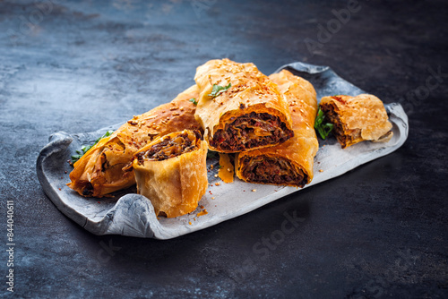 Traditional Turkish crispy sigara borek rolls with minced meat rolled in fillo pastry served as close-up in a Nordic design tray on a black board photo