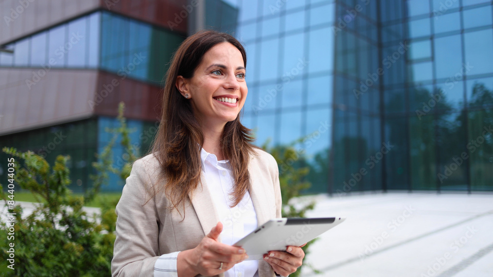 Beautiful, young businesswoman enjoying outside, in front of her company building and using a digital tablet Beautiful, young businesswoman enjoying outside, in front of her company building and using a digital tablet