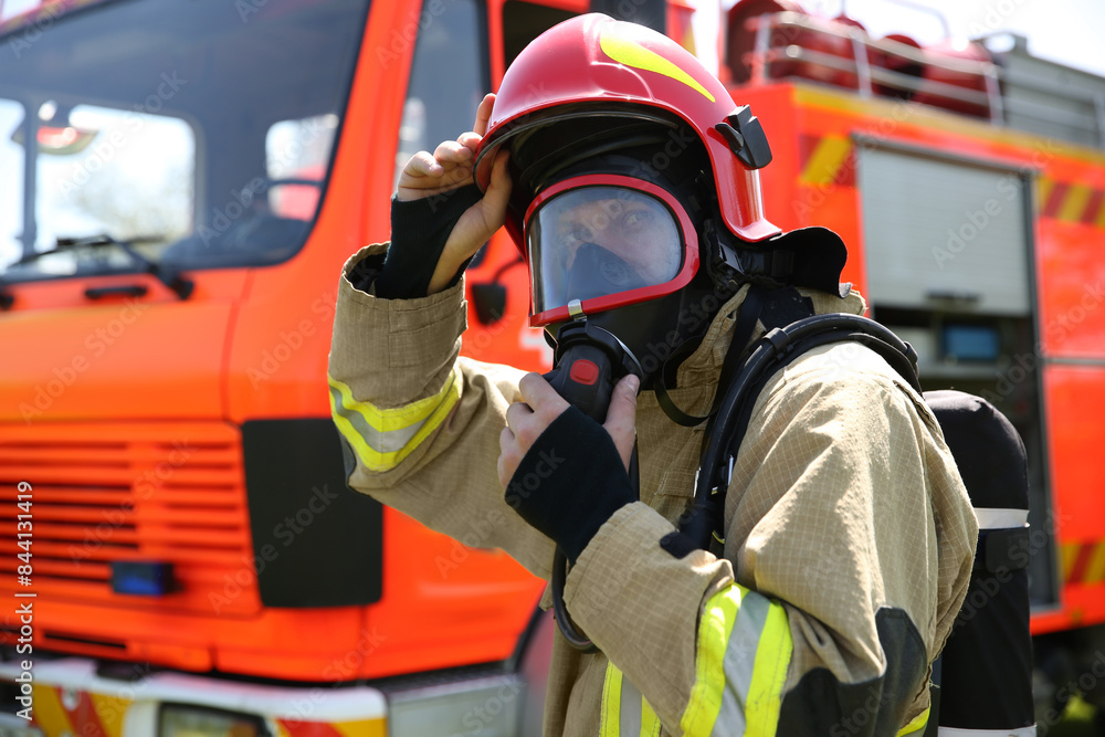 Firefighter in uniform wearing helmet and mask near fire truck outdoors Firefighter in uniform wearing helmet and mask near fire truck outdoors