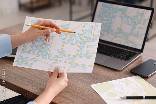 Cartographer working with cadastral maps at wooden table in office, closeup