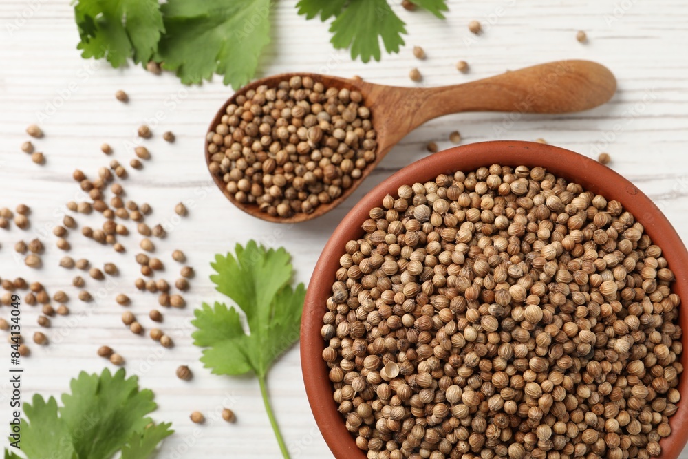 Dried coriander seeds in bowl, spoon and green leaves on wooden table, flat lay Dried coriander seeds in bowl, spoon and green leaves on wooden table, flat lay