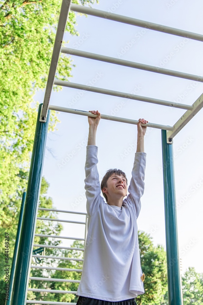 Young Man Doing Pull Ups on Outdoor Gym Equipment During Summer Day Young Man Doing Pull Ups on Outdoor Gym Equipment During Summer Day