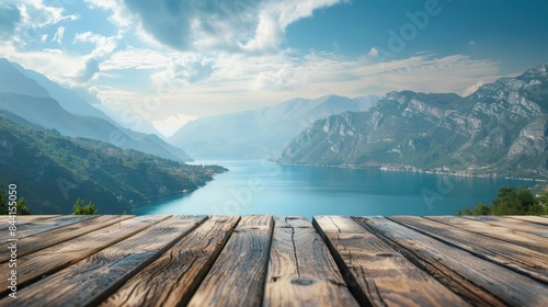 Scenic view of a tranquil lake surrounded by majestic mountains, with a wooden deck in the foreground under a cloudy blue sky. © narak0rn